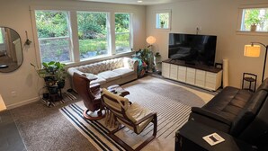 En stue med sofa, stole, fjernsyn og store vinduer.