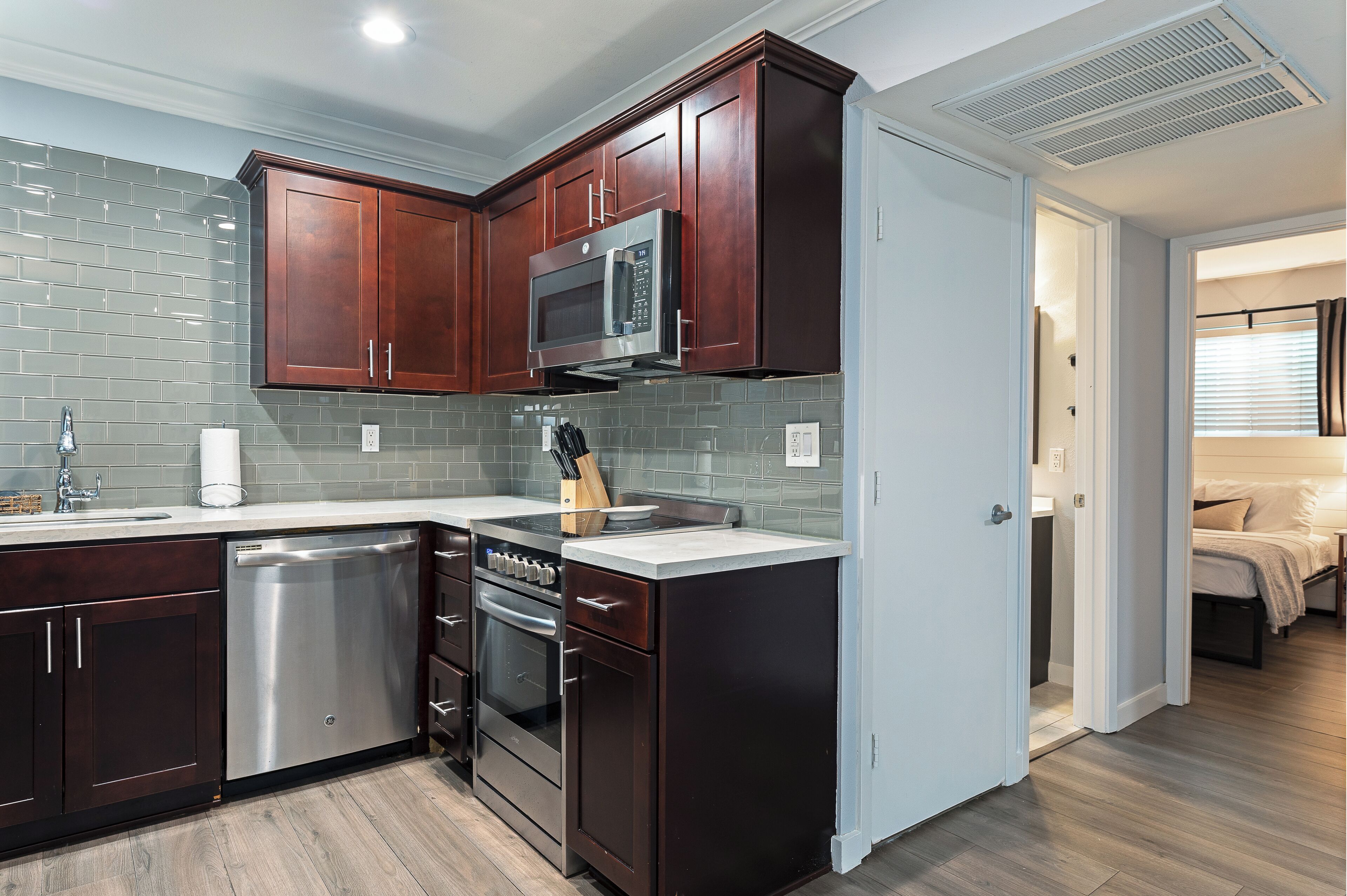 A compact kitchen with dark wood cabinets, a stainless steel dishwasher, and a microwave.