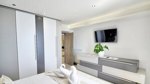 Quarto moderno com cama grande, guarda-roupa, penteadeira com espelho e um vaso com planta.