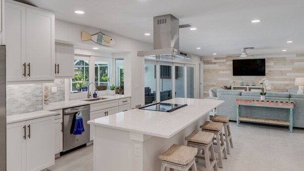Una cocina moderna con armarios blancos, una isla grande y un área de comedor con sofá y taburetes de bar.