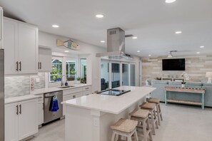 Une cuisine moderne avec des meubles blancs, un grand îlot central et un coin repas comprenant un canapé et des tabourets de bar.