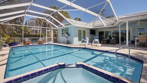 Una piscina con cerramiento de vidrio, sillas de descanso y un área de patio con mobiliario exterior.