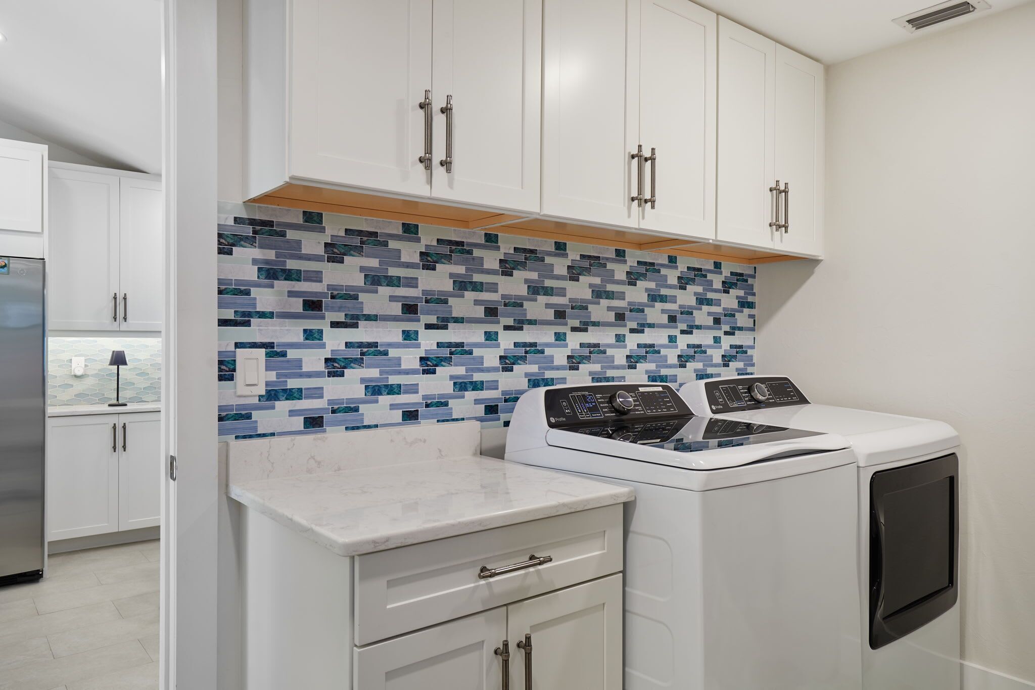 Uma lavanderia com máquina de lavar e secadora, armários brancos e painel de azulejos.