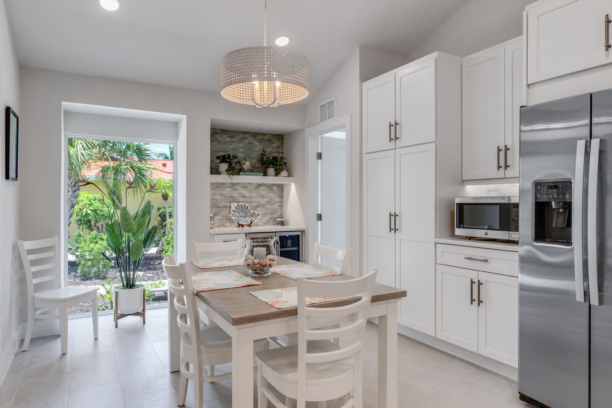 A modern kitchen with white cabinets, a stainless steel refrigerator, a microwave, and a dining area with a wooden table and chairs.