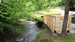 Une terrasse en bois surplombant un ruisseau, avec un sentier en pierre et une zone herbeuse.