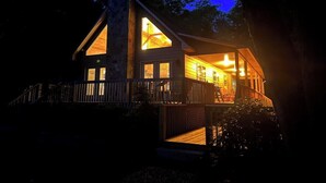 Une cabane dotée d’une grande fenêtre centrale, d’une terrasse et d’une cheminée.