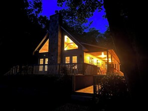 A cabin with a large central window, a deck, and a chimney. - Creek Front Lodge • Private Setting • Fast Internet • Firepit (Hayesville)