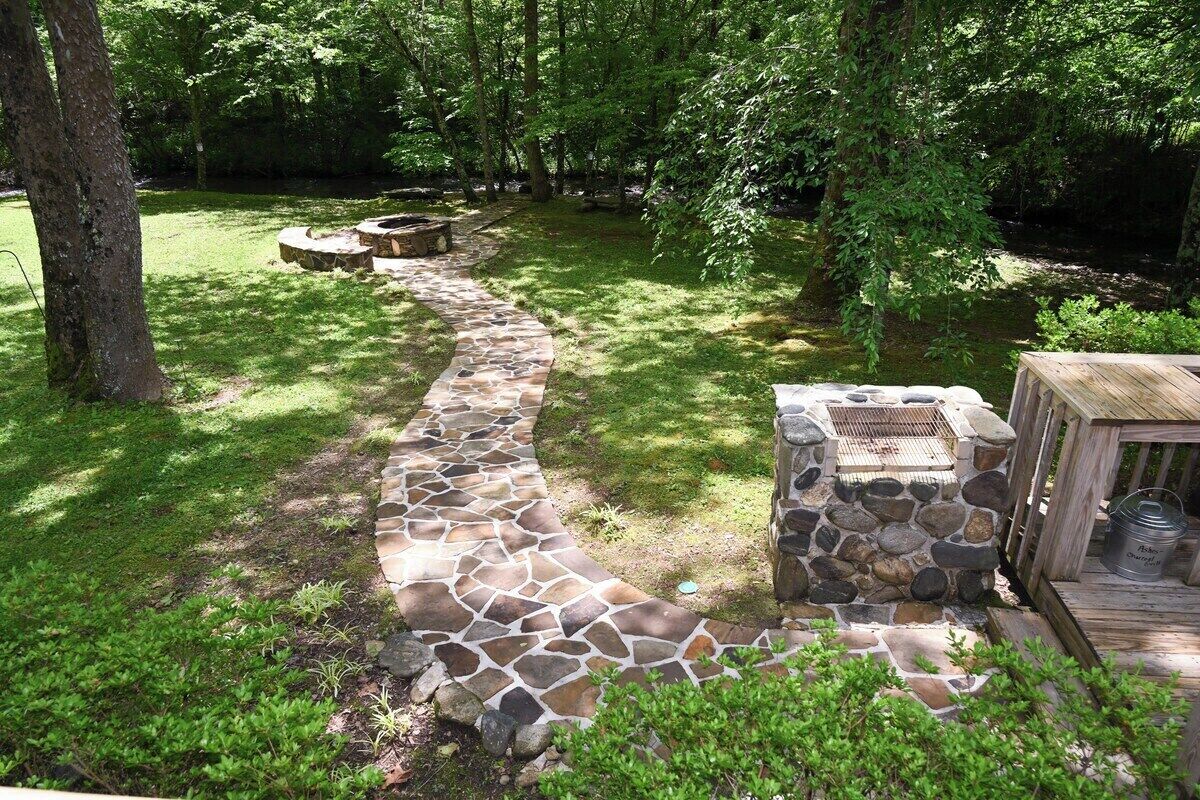 A stone pathway leading to a stone barbecue area surrounded by lush greenery.