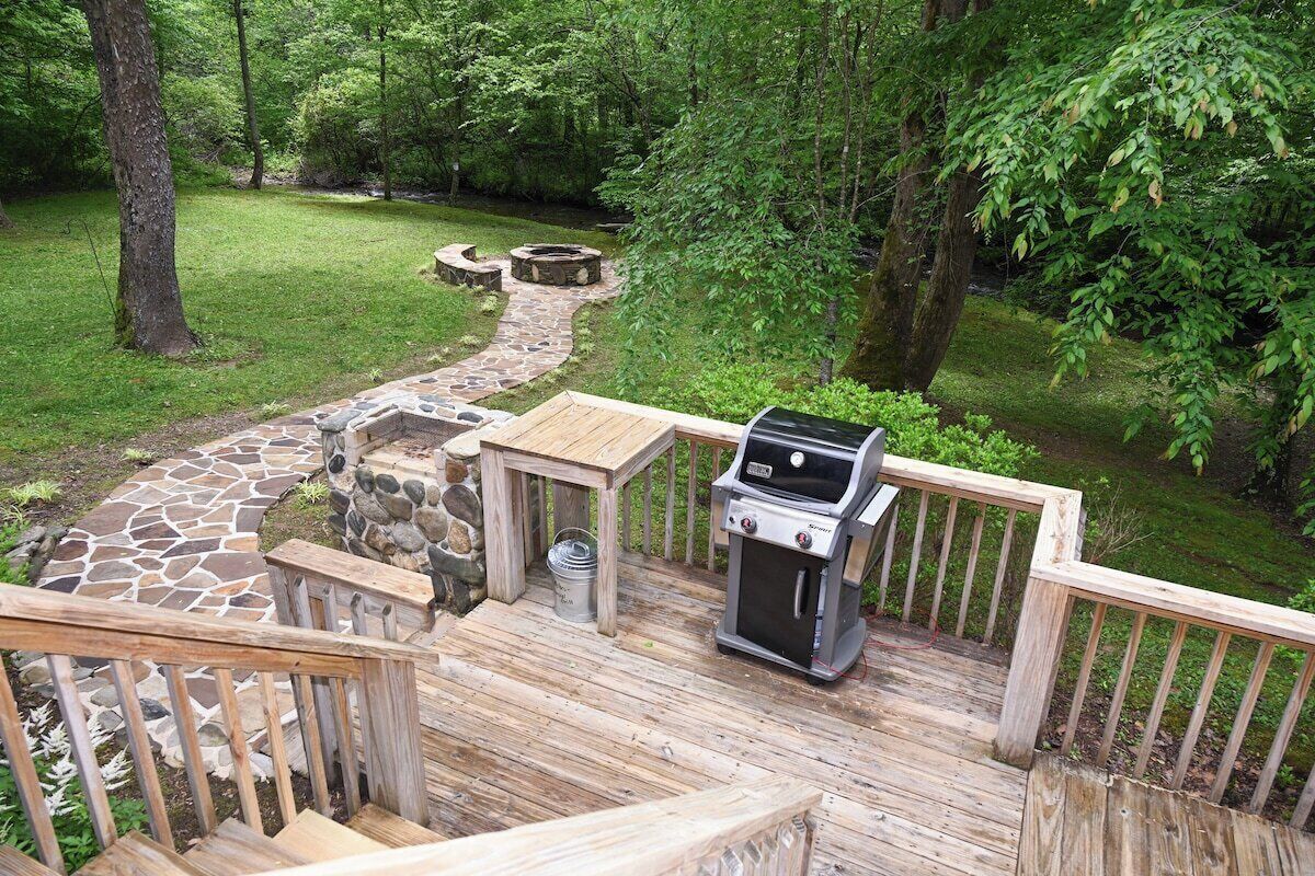 A deck with a grill, stone pathway, and a small table.