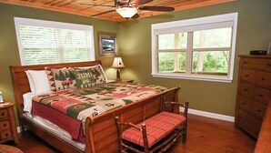 Une chambre à coucher avec un lit en bois, un banc, une table de chevet, une commode et une fenêtre donnant sur un paysage verdoyant.