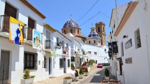 Uma rua estreita com edifícios brancos, uma igreja com cúpula e mesas ao ar livre.