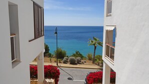 Uma rua estreita com edifícios brancos, vista clara do mar e flores vermelhas ao longo da calçada.