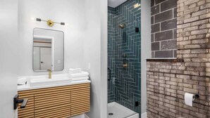Un bany modern amb un lavabo blanc, dutxa amb envidriament i una paret decorativa de maó.