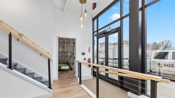 Un interior modern amb una escala, tarima de fusta i grans finestres que ofereixen vistes a l'exterior.
