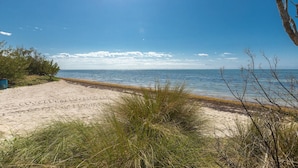 Une plage avec du sable, de l’herbe et un ciel dégagé.