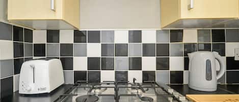 A kitchen with a gas stove, a toaster, and a kettle.