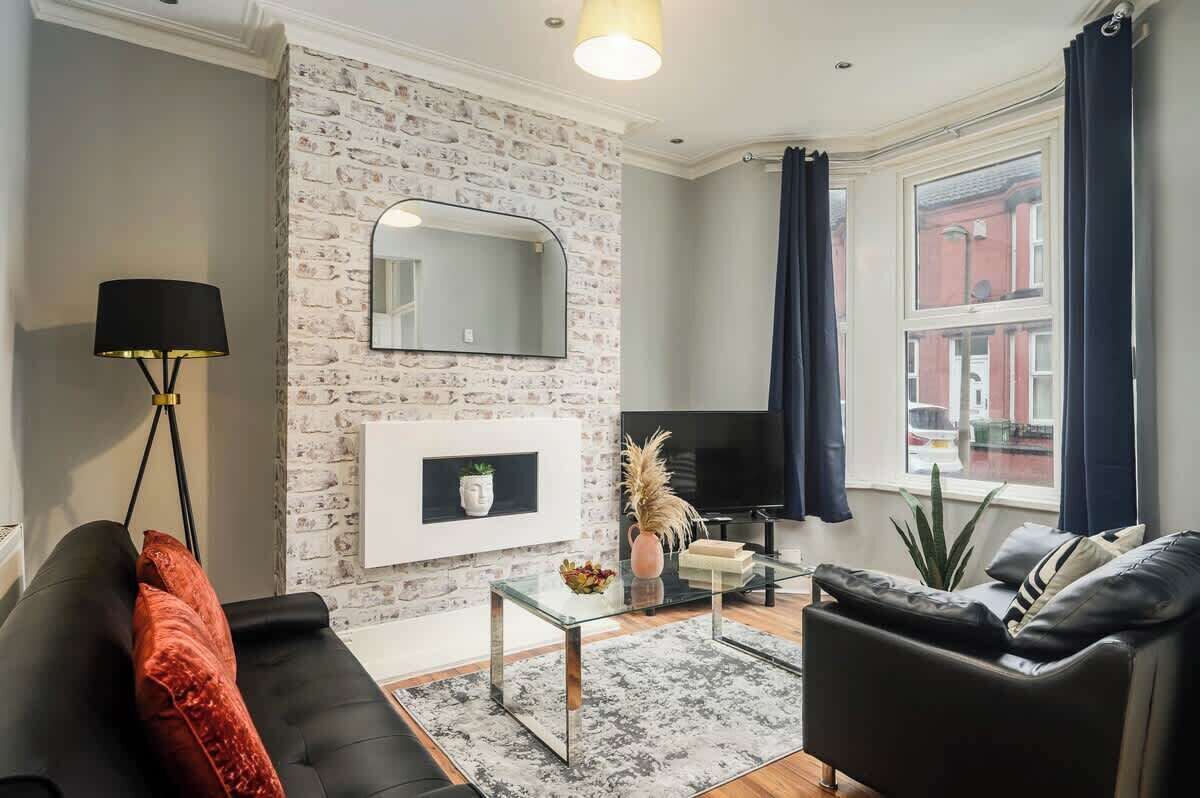 A modern living room with a stone wall, a flat-screen TV, a glass coffee table, and a black leather sofa.