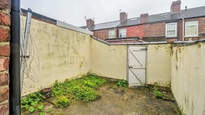 A narrow alleyway with a small door, overgrown vegetation, and a brick wall. - Willow House - 2-Bedroom House In Merseyside (Merseyside)