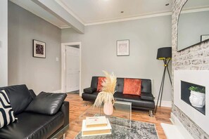 A modern living room with a black leather sofa, a glass coffee table, and a fireplace with a white mantel.