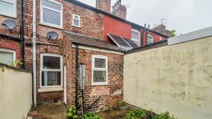 A narrow alleyway with a brick building, a small garden, and a solar panel on the roof. - Willow House - 2-Bedroom House In Merseyside (Merseyside)