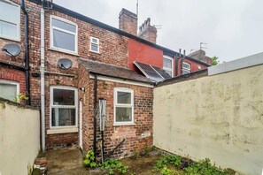 A narrow alleyway with a brick building, a small garden, and a solar panel on the roof. - Willow House - 2-Bedroom House In Merseyside (Merseyside)