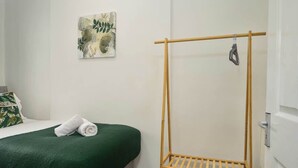 A room with a bed, a green blanket, a wooden drying rack, and a wall-mounted artwork. - Willow House - 2-Bedroom House In Merseyside (Merseyside)