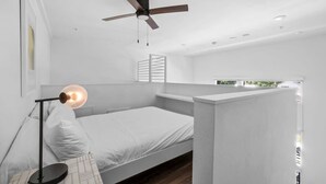 Quarto moderno com uma cama de solteiro, um ventilador de teto, um abajur e vista para o verde lá fora.