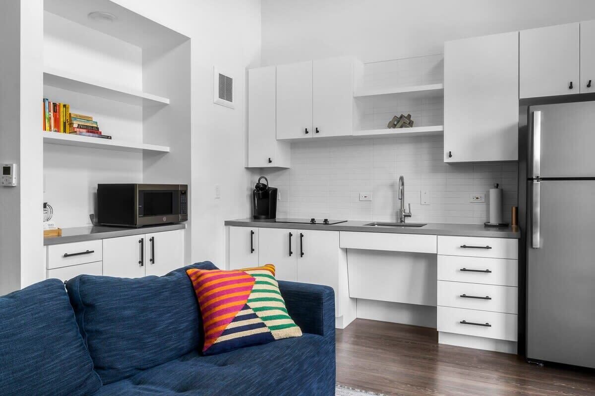 A modern kitchen with white cabinets, a stainless steel refrigerator, a microwave, and a coffee maker.