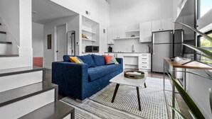 Uma cozinha moderna com armários brancos, um sofá azul e uma sala de jantar com mesa e cadeiras.