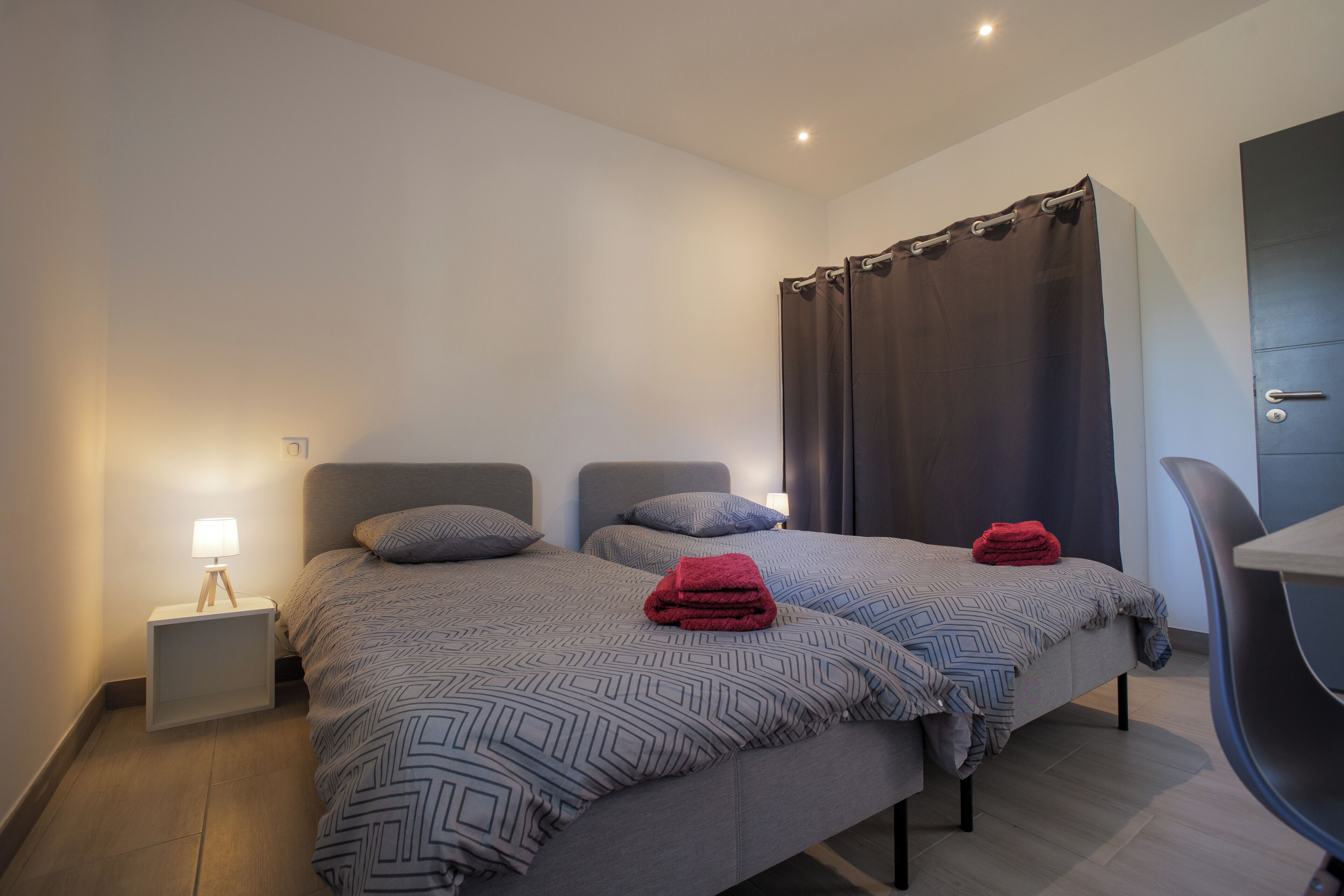 Een moderne hotelkamer met twee bedden, een bureau en een stoel.