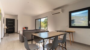 A modern living room with a dining area, a sofa, and a large window with a view of the outdoors. - Casa Léa (Sollacaro)