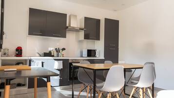 Een moderne keuken met donkere kastjes, een magnetron en een koffiezetapparaat. Er staat een houten tafel met vier stoelen.