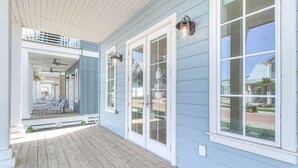 A covered porch with a wooden deck, white-framed glass doors, and wall-mounted lanterns. - 3-story home near the beach with outdoor pool, golf, deck, grill, streaming, W/D (Port Aransas)