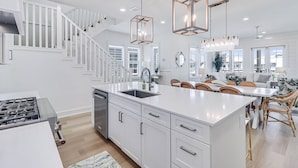 A modern kitchen with white cabinetry, a central island, and pendant lighting. - 3-story home near the beach with outdoor pool, golf, deck, grill, streaming, W/D (Port Aransas)