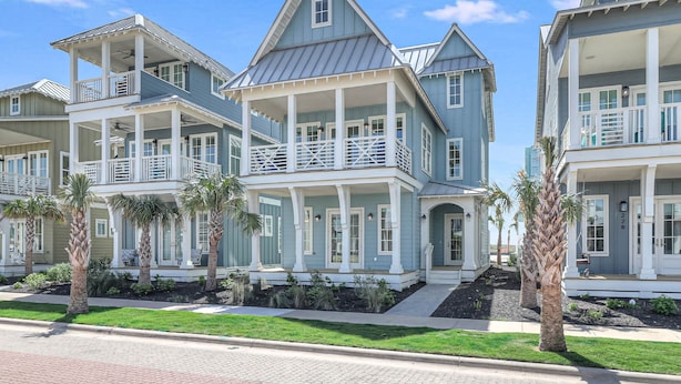A coastal-style multi-story house with a balcony, a covered porch, and a well-maintained lawn with palm trees. - 3-story home near the beach with outdoor pool, golf, deck, grill, streaming, W/D (Port Aransas)