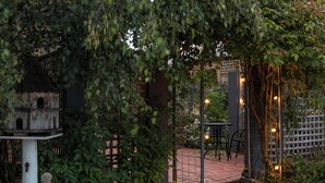 En havepatio med pergola, fuglehus og en brobelagt sti.