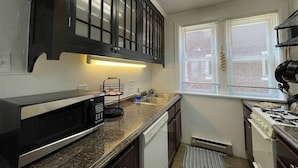 A compact kitchen with dark wooden cabinets, a stainless steel microwave, a gas stove, and a window with blinds.