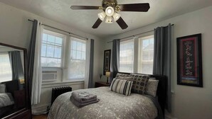 A bedroom with a large bed, a ceiling fan, and two windows with curtains.