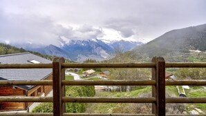 Une vue sur une montagne, avec une clôture en bois au premier plan, un bâtiment doté d’un toit en pente et des montagnes enneigées en arrière-plan.