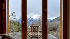 Une porte à ossature en bois donnant sur un patio équipé d’une table et de chaises, d’où l’on peut admirer un paysage montagneux.