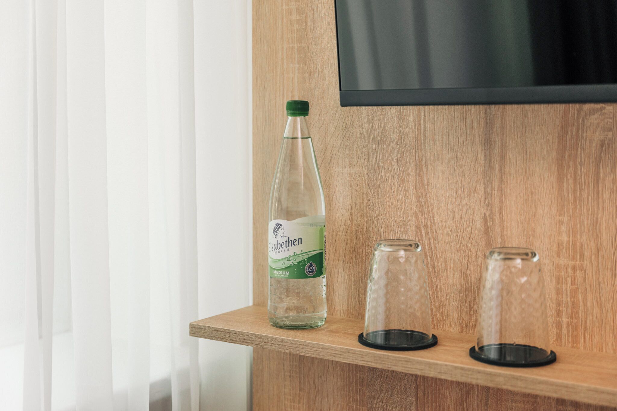 A bottle of Isabellen medium on a wooden shelf with two empty glasses.