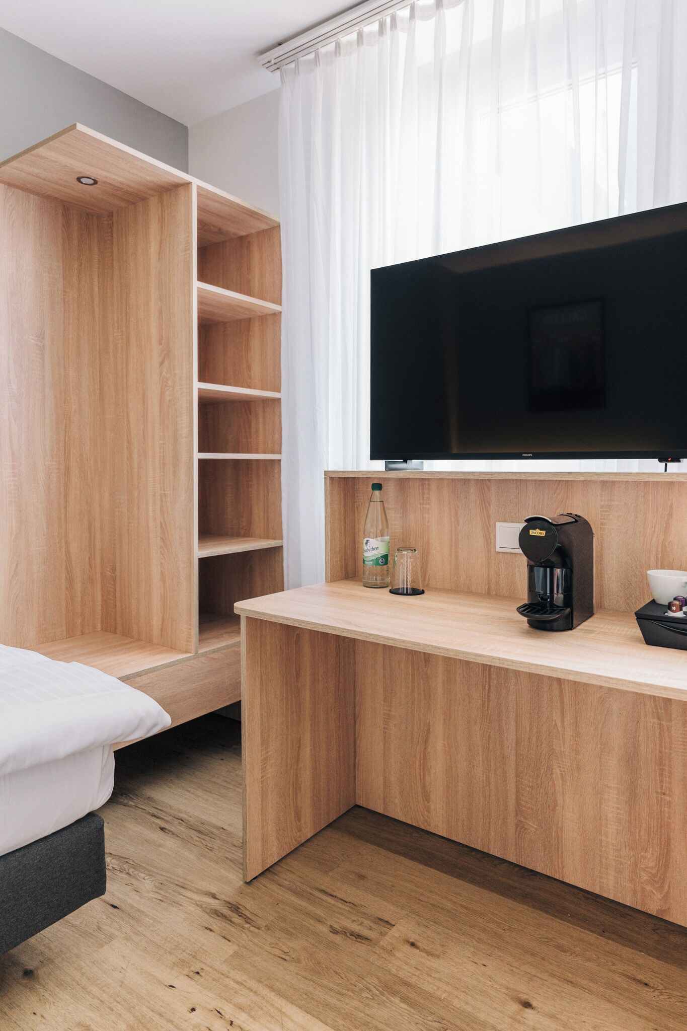Habitació d'hotel moderna amb escriptori de fusta, televisió de pantalla plana, cafetera i llit.