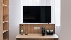 Una habitación moderna con un escritorio de madera, un televisor de pantalla plana, una botella de agua, un vaso, una cafetera y tazas.