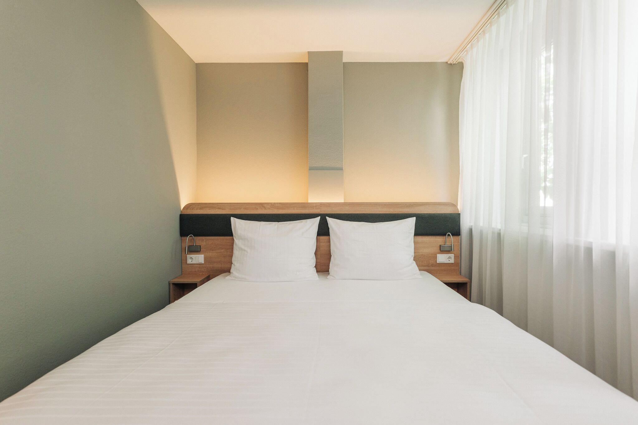 A hotel room with a large bed, two bedside tables, a nightstand, and a headboard with a light fixture.