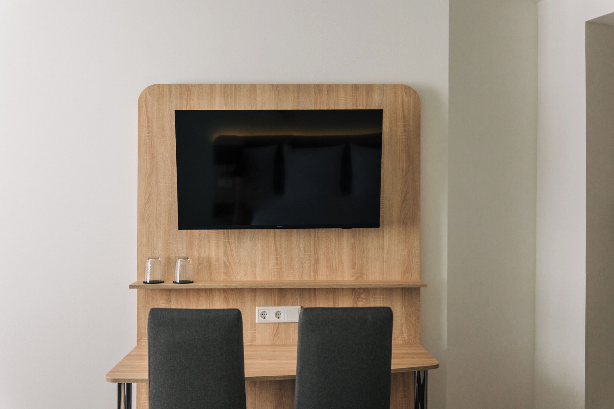 Ein modernes Zimmer mit einer Holz-TV-Konsole, einem Flachbildfernseher, zwei Stühlen und einem kleinen Tisch.