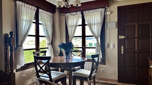 Un comedor con una mesa redonda, cuatro sillas, un florero con flores y dos ventanas con cortinas.