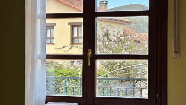 Una habitación con cama, ventana y balcón con vistas a edificios.
