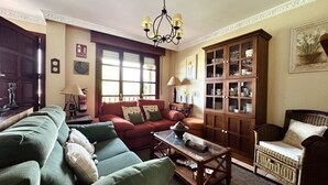 Una sala de estar acogedora con un sofá verde, un sofá rojo, un sillón de mimbre y un mueble de madera con puertas de cristal.
