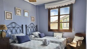 Una habitación con dos camas, una silla de madera y un ventanal con vistas a edificios.