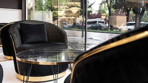Un interior moderno con un sofá tapizado en negro y una mesa de vidrio, amplias ventanas con vistas a coches aparcados y árboles.